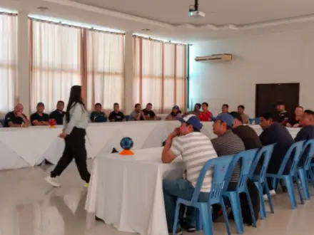 Salón con mesas en U durante un taller; la facilitadora recorre el centro.