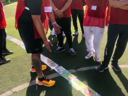 Equipo con chalecos rojos coordinando los pies sobre una cinta en la cancha.